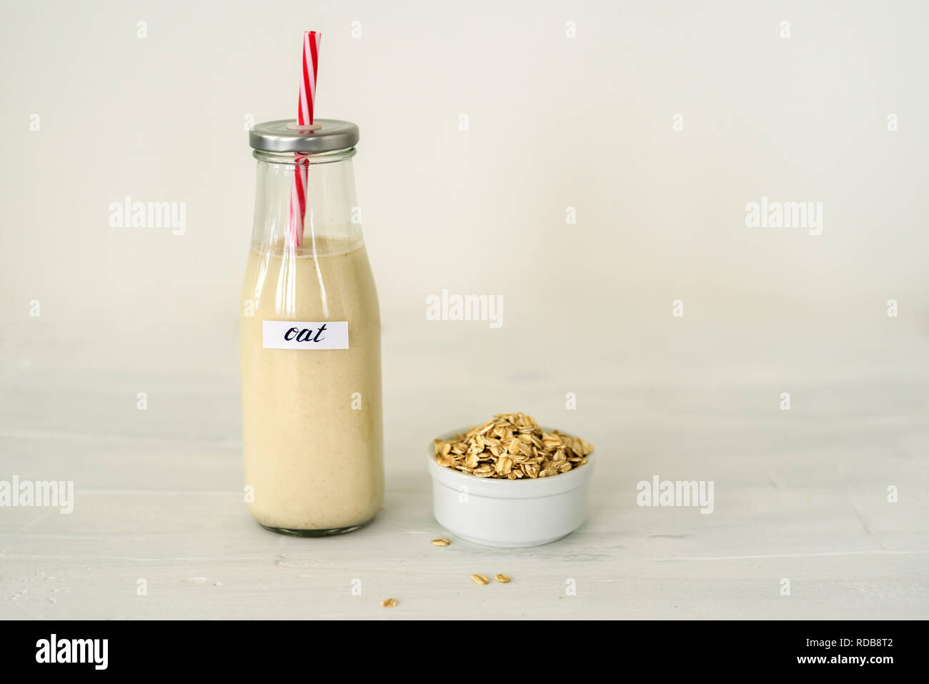 Bottiglia di vetro di latte di avena su sfondo bianco. Ciotola con fiocchi di avena vicino ad essa Foto Stock