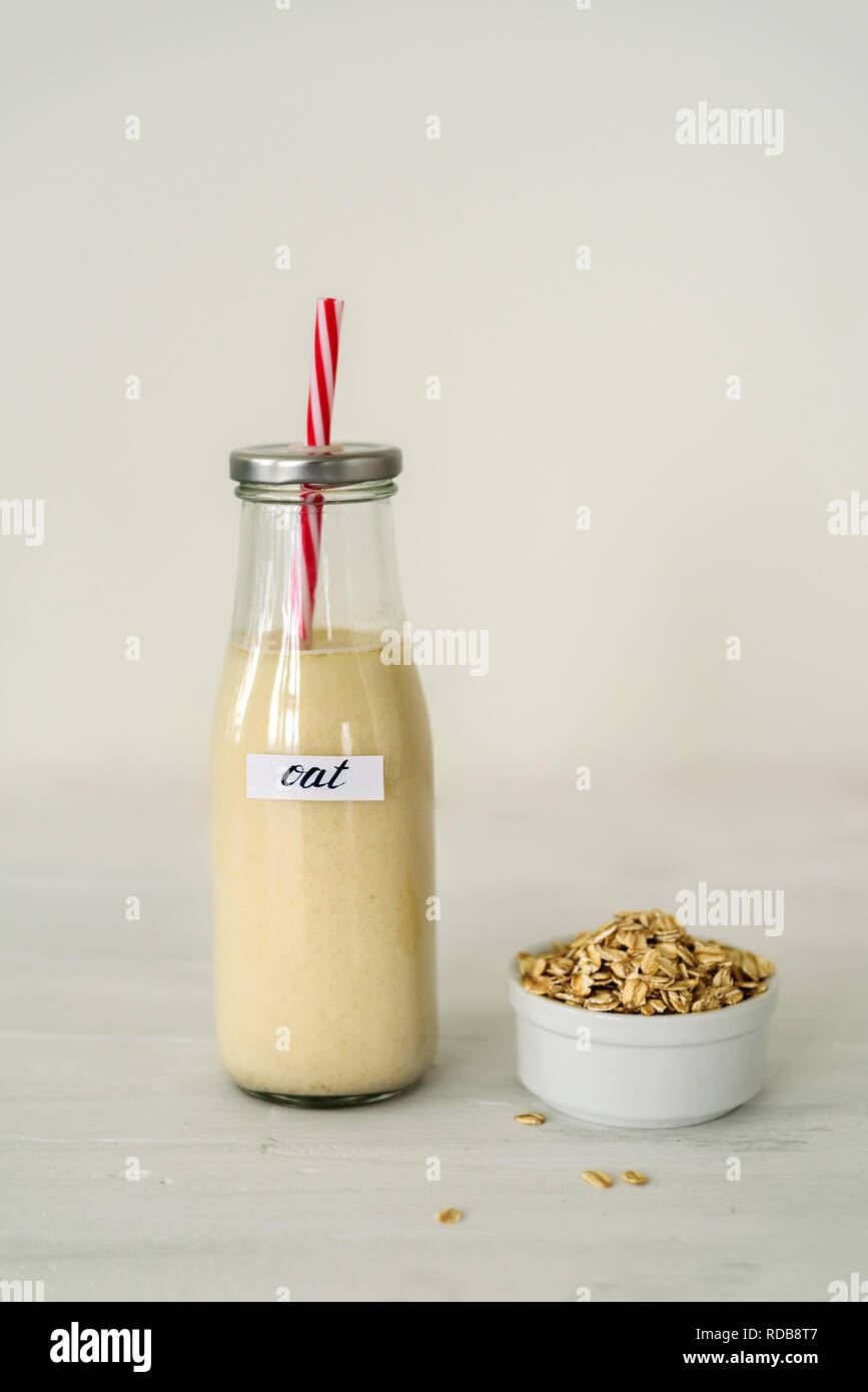 Bottiglia di vetro di latte di avena su sfondo bianco. Ciotola con fiocchi di avena vicino ad essa Foto Stock