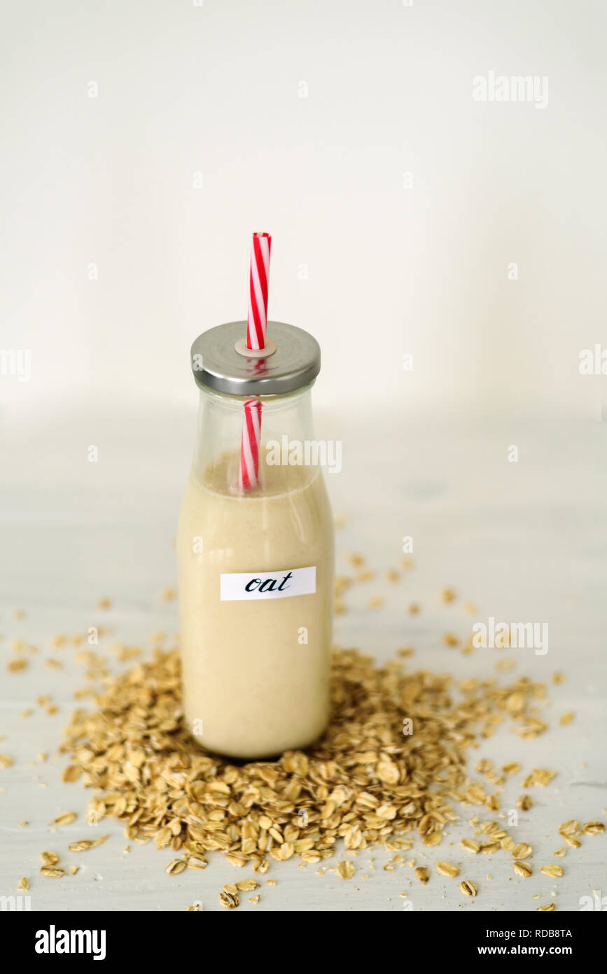 Bottiglia di vetro di latte di avena su sfondo bianco dietro mucchio di fiocchi di avena Foto Stock