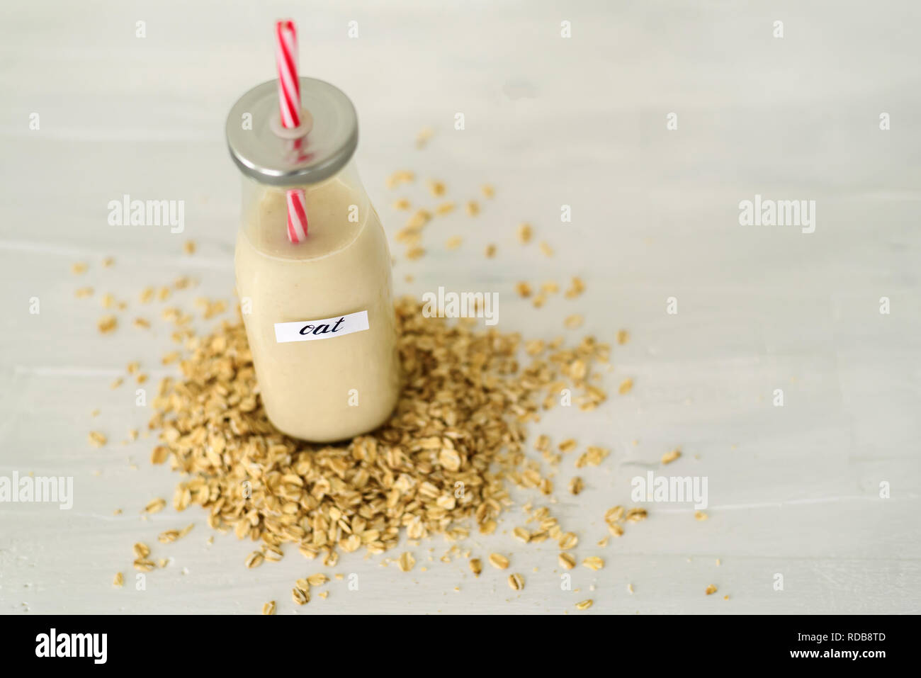 Bottiglia di vetro di latte di avena su sfondo bianco dietro mucchio di fiocchi di avena Foto Stock