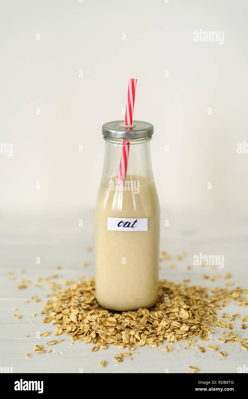 Bottiglia di vetro di latte di avena su sfondo bianco dietro mucchio di fiocchi di avena Foto Stock