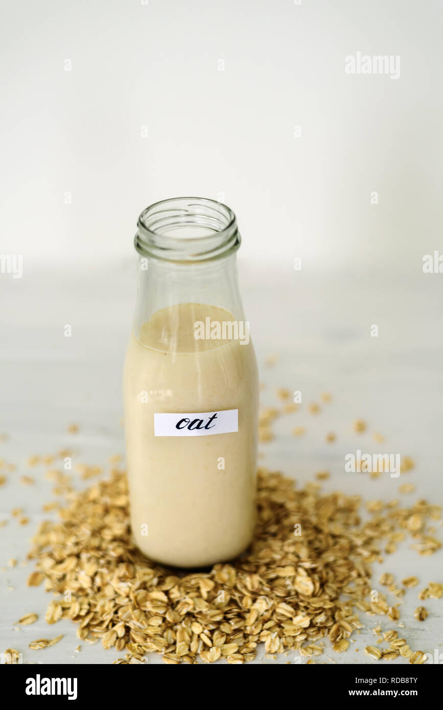 Bottiglia di vetro di latte di avena su sfondo bianco dietro mucchio di fiocchi di avena Foto Stock