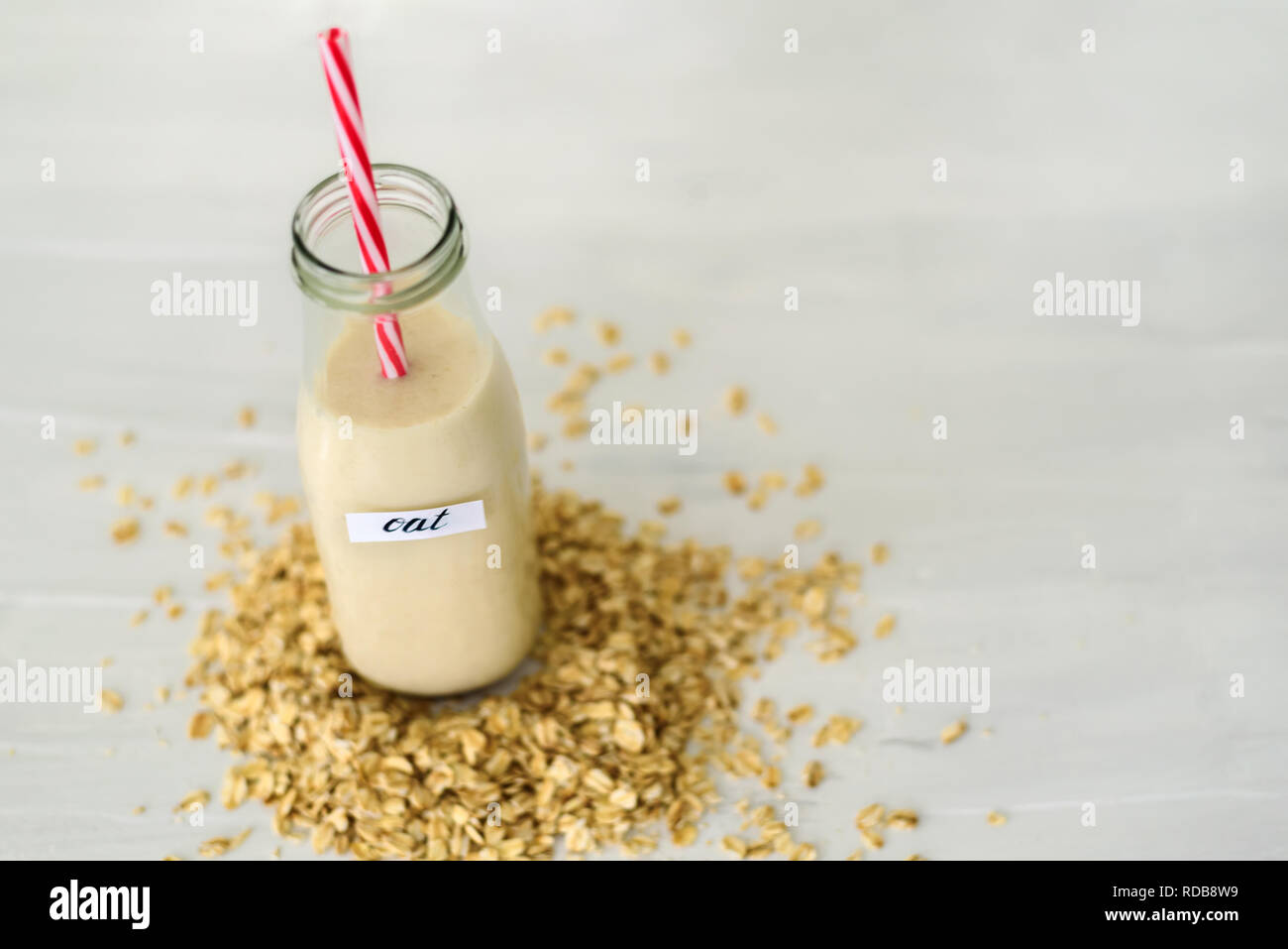 Bottiglia di vetro di latte di avena su sfondo bianco dietro mucchio di fiocchi di avena Foto Stock