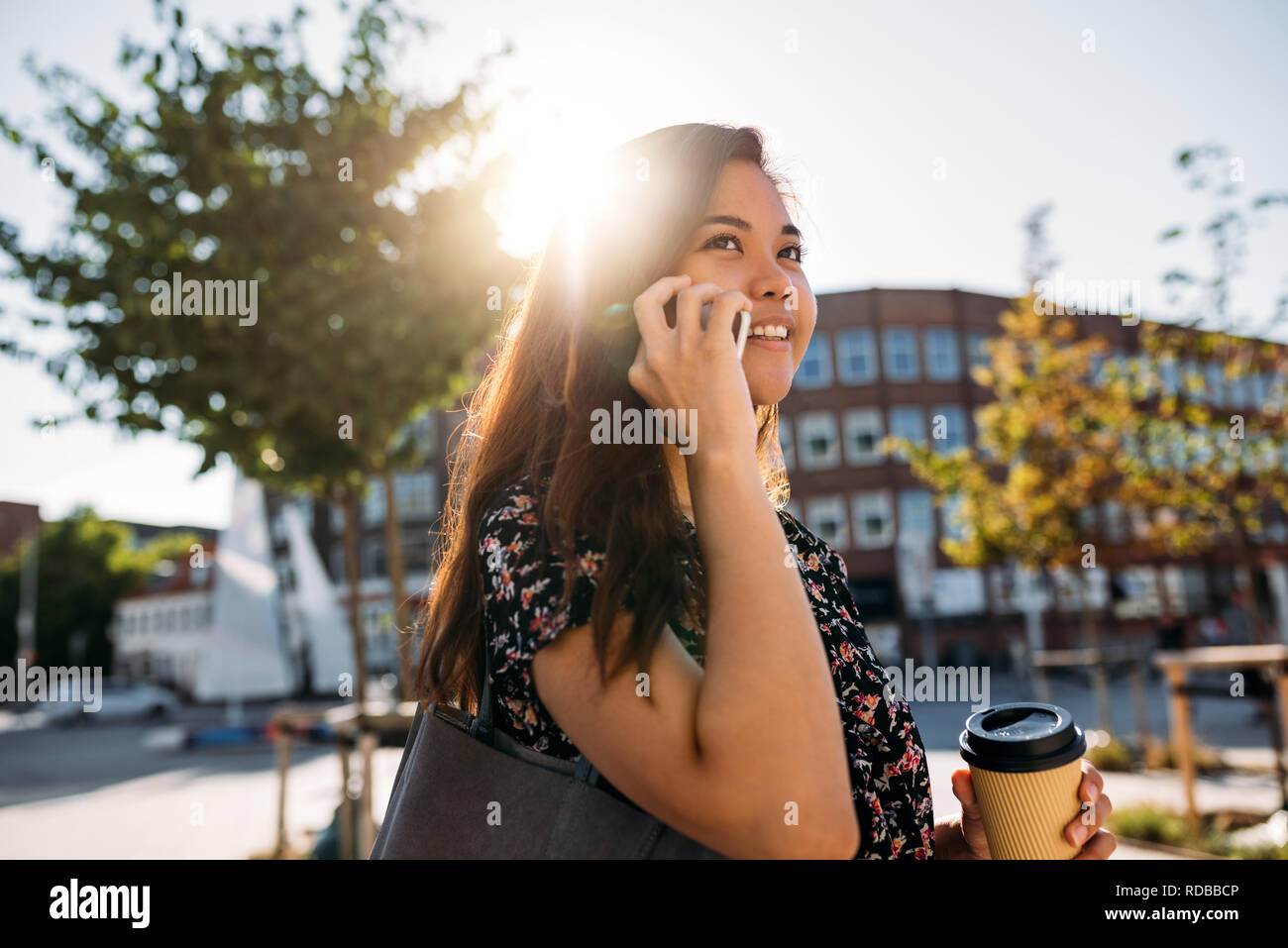 Sorridente Asian studente universitario a camminare e parlare sul suo cellulare Foto Stock