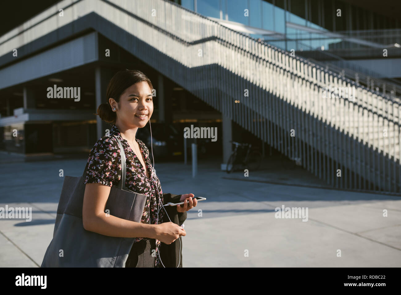 Sorridente Asian studente universitario camminando sul campus ascolto di musica Foto Stock