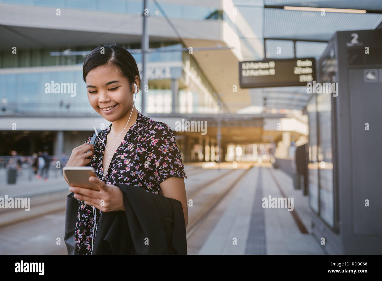 Sorridente studente asiatico sta in piedi in una fermata del tram la lettura di testi Foto Stock