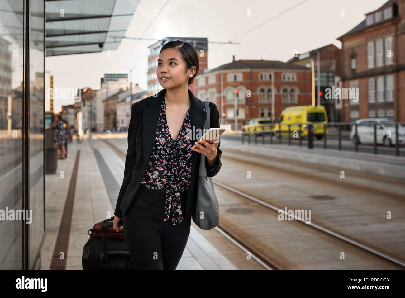 Imprenditrice asiatici in attesa con i suoi bagagli in corrispondenza di una fermata del tram Foto Stock