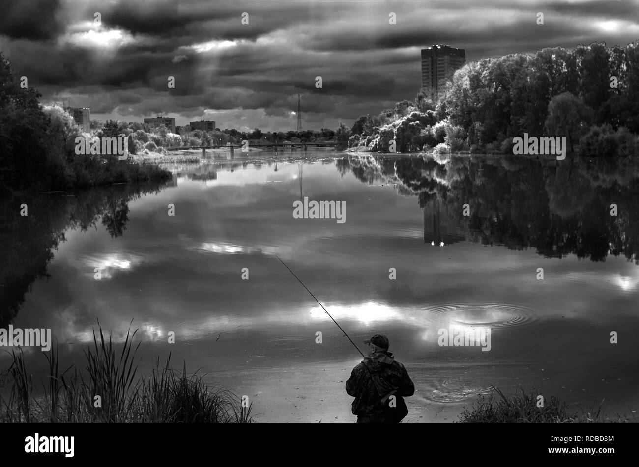 Pescatore solitario su di una tranquilla ampio fiume. Giornata di sole mette in evidenza le riflessioni su una superficie liscia acqua calma. Sole brillante luce sky tree forest. Fisher con asta sulla riva. Russia Mosca area paesaggio natura Foto Stock