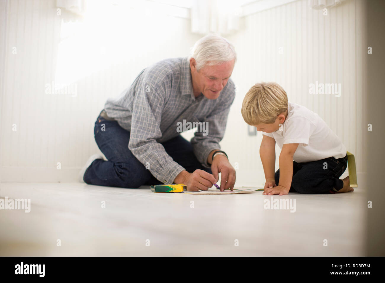 Nonno e nipote di Disegno con matite colorate mentre inginocchiati sul pavimento. Foto Stock