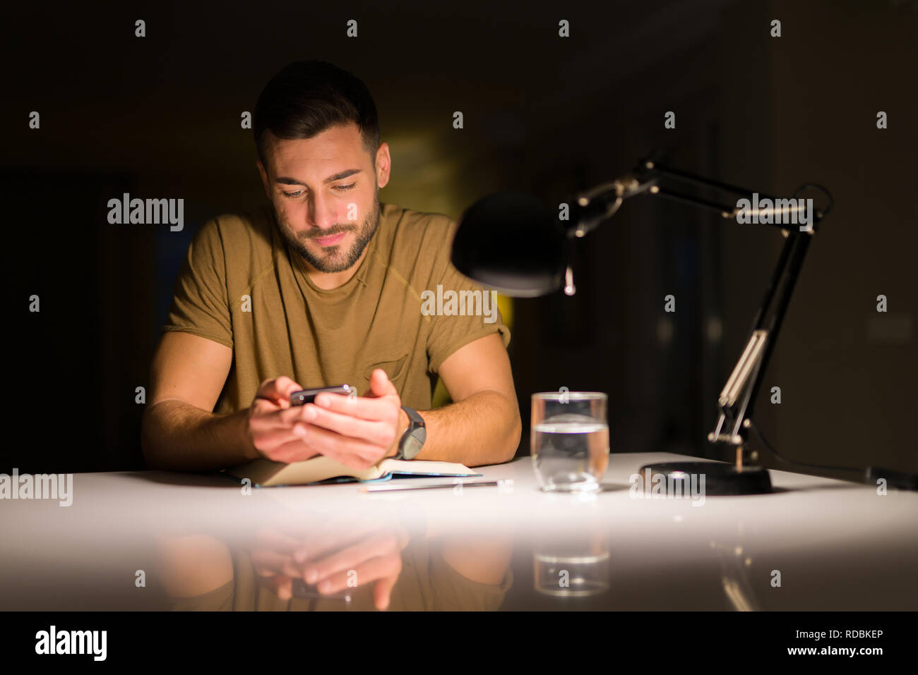 Giovane uomo bello studiare a casa , utilizzando lo smartphone, guardando il telefono sorridente Foto Stock