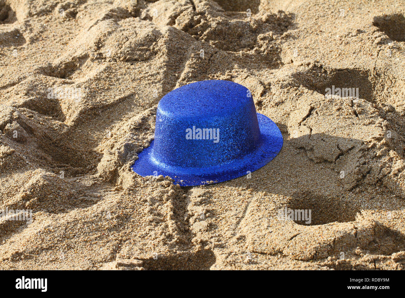 Blue glittery party hat abbandonati sulla spiaggia dopo una celebrazione o una festa Foto Stock