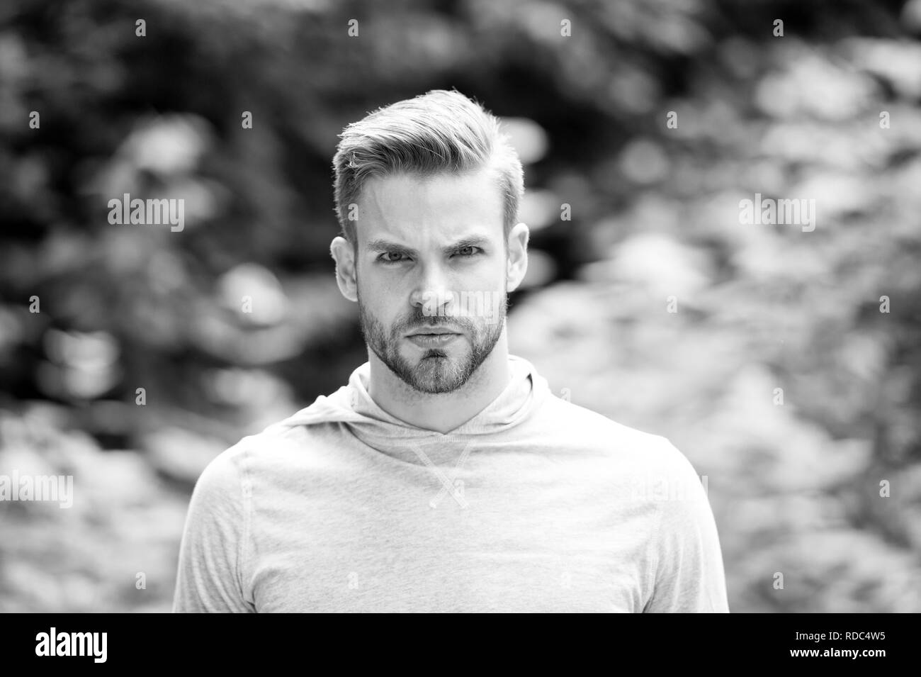 Guy barbuto e attraente si preoccupa di aspetto. Uomo con setole gravi sul viso, natura verde, sfondo sfocato. Concetto Metrosexual. Uomo con barba o barba lunga ragazzo sembra bello e fresco. Foto Stock