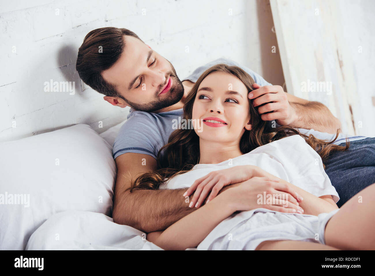 Adulto Giovane amorevole abbraccio dolce in camera da letto mentre l uomo di toccare i capelli della donna Foto Stock