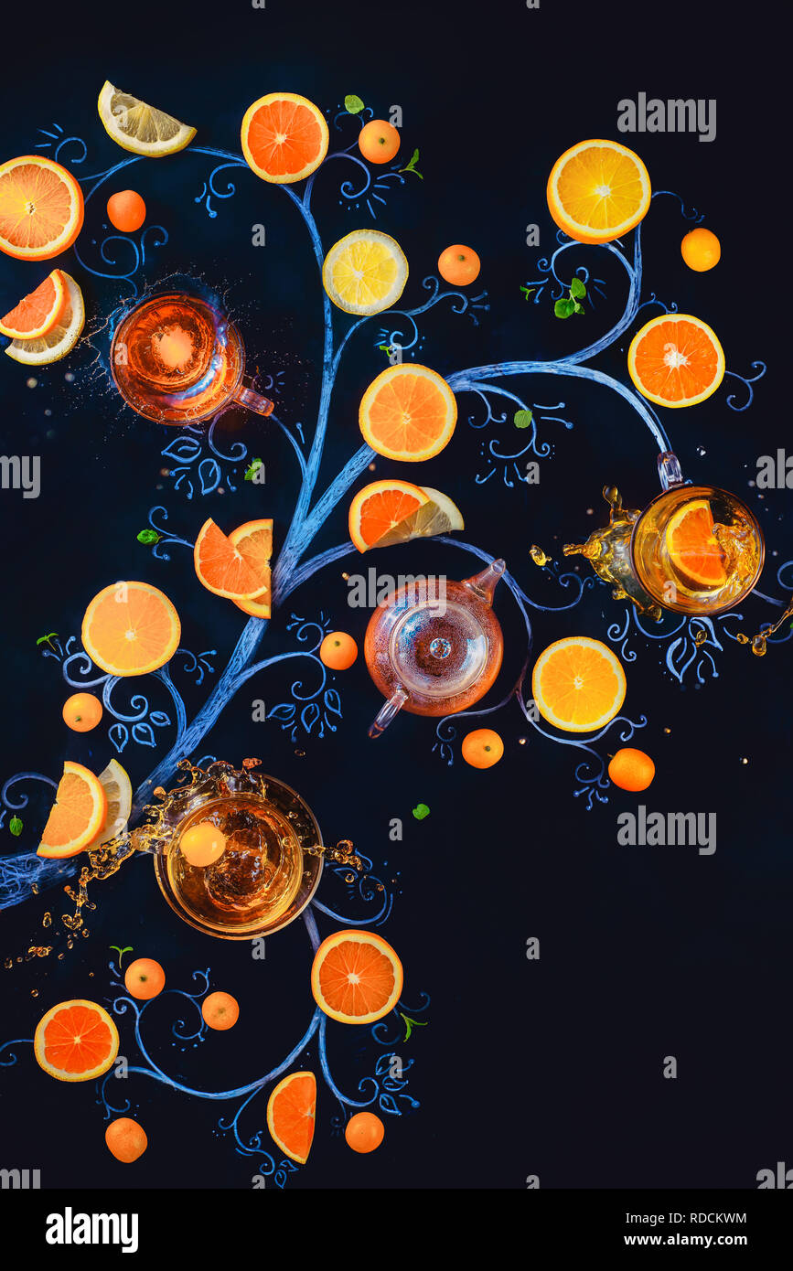 Tè al limone chalk tree con teacups, teiera e fette di arance e di limoni. Bevanda calda creative laici piatta con spruzzi su sfondo scuro con spazio di copia Foto Stock