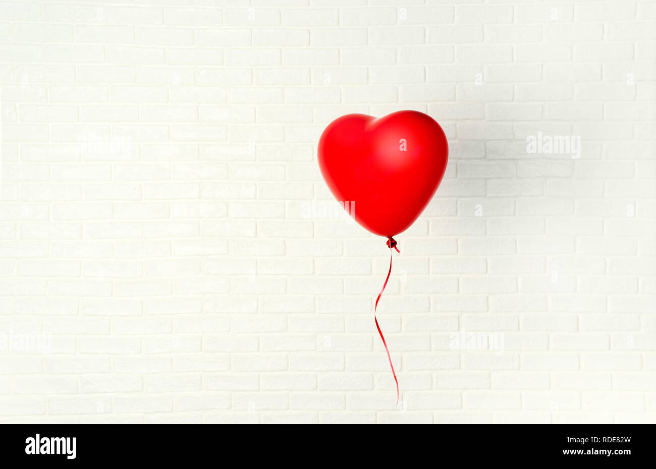 Red ballon con forma di cuore pende aganst muro bianco Foto Stock