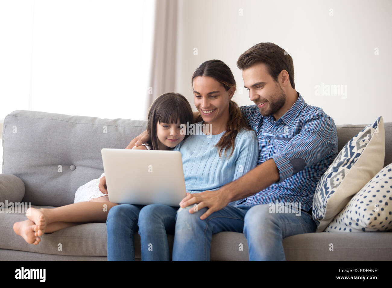La famiglia felice con la figlia di capretto divertitevi con il portatile a casa Foto Stock