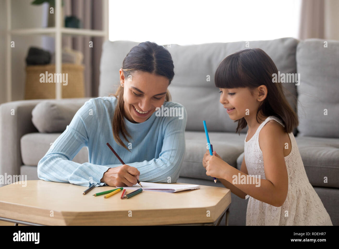 Sorridente madre aiutare la ragazza in età prescolare insegnamento carino kid per disegnare Foto Stock