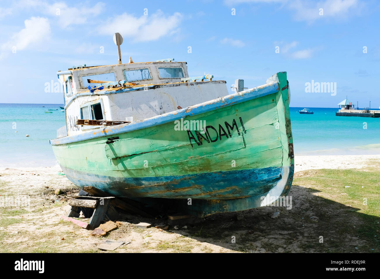 Un di legno barca da pesca in verde e blu vernice peeling, che è visto giorni migliori, è su una spiaggia dei Caraibi in attesa di riparazioni che non può mai venire Foto Stock