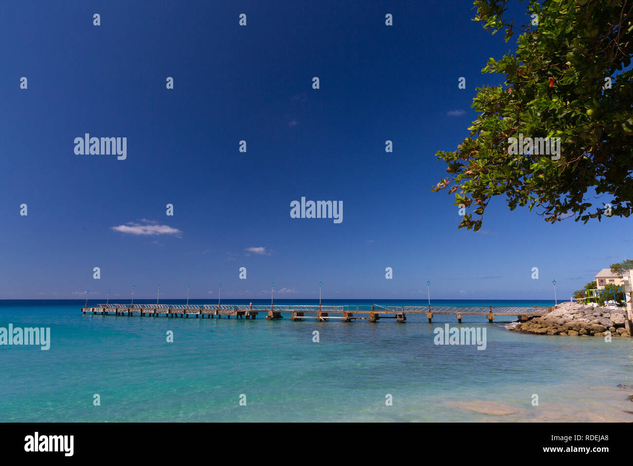 Il molo a Mullins Beach, Barbados si allunga in un mare turchese sotto un cielo blu chiaro. Foto Stock