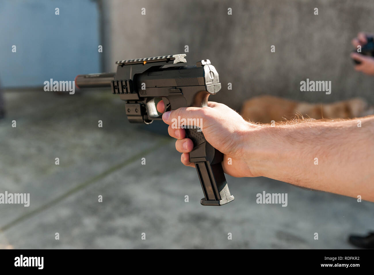 Close up della persona bianca il braccio con la mano che regge il nero pistola giocattolo all'aperto durante la giornata di sole Foto Stock