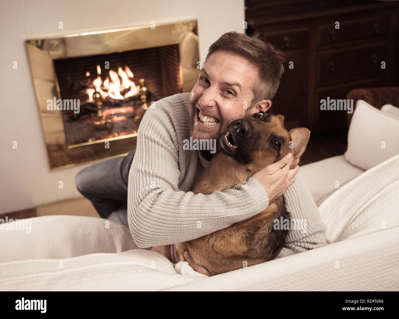 Bel ritratto di uomo sorridente abbracciando il cane pastore tedesco giocando insieme davanti al camino a casa accogliente in giornata invernale in felicità Friendshi Foto Stock