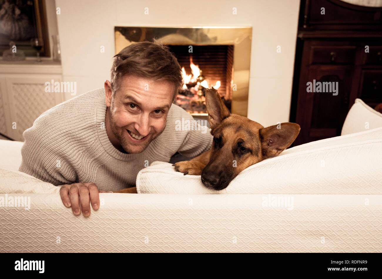Bel ritratto di uomo sorridente abbracciando il cane pastore tedesco giocando insieme davanti al camino a casa accogliente in giornata invernale in felicità Friendshi Foto Stock