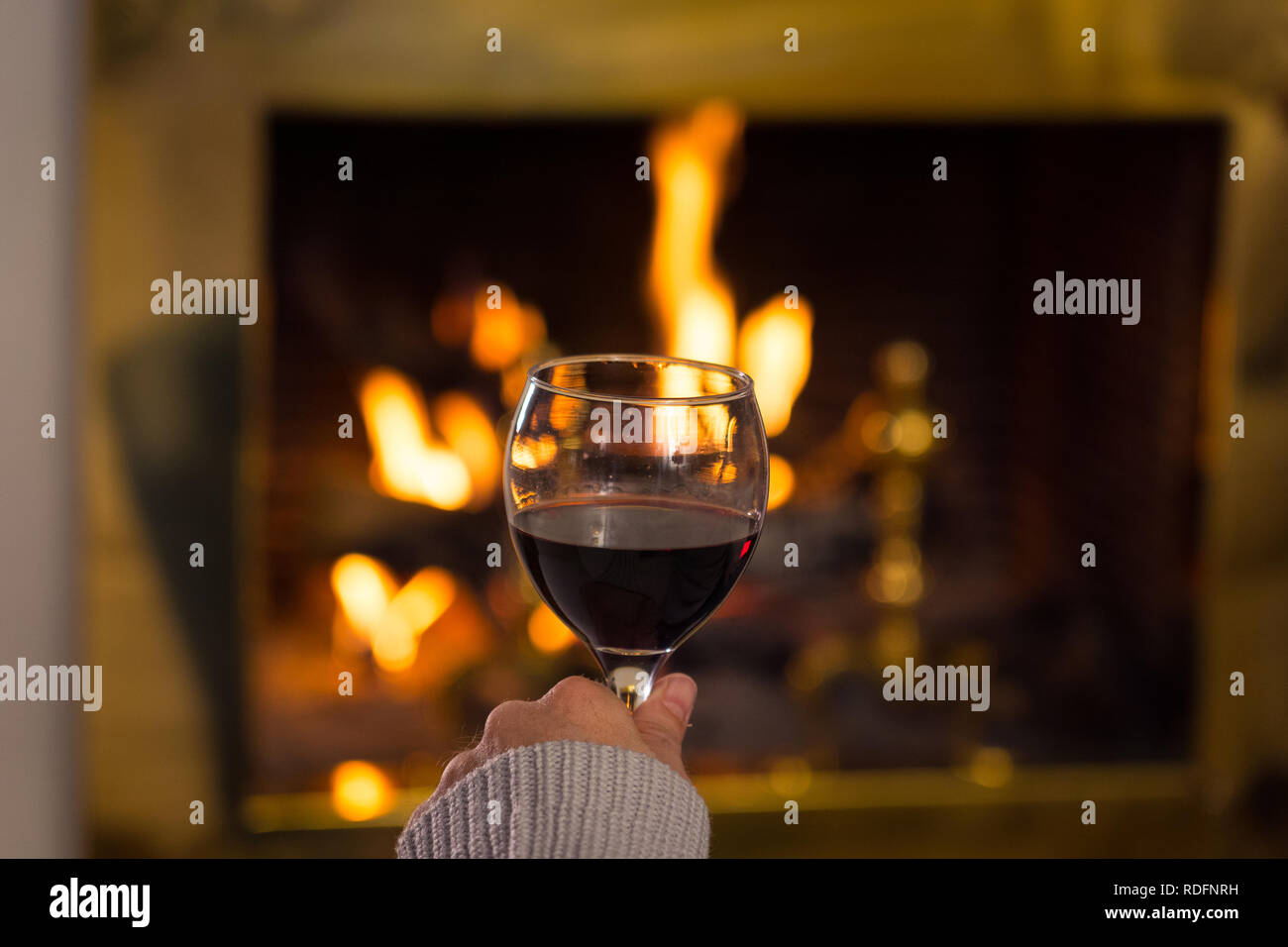 Close up uomo holding e di bere il vino rosso il vetro da fuoco di legno aperto posto rilassante e piacevole momento di quiete a casa in vacanza invernale vacanza, Chr Foto Stock