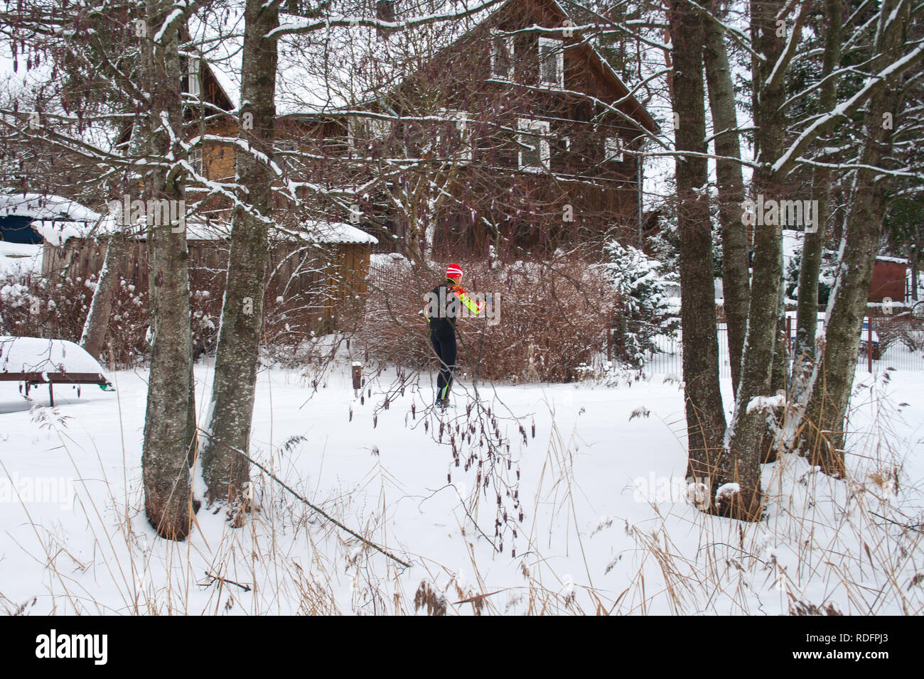 Casa in legno sul lago ghiacciato, barca, alberi e canne ricoperte di neve, sci di persone Foto Stock