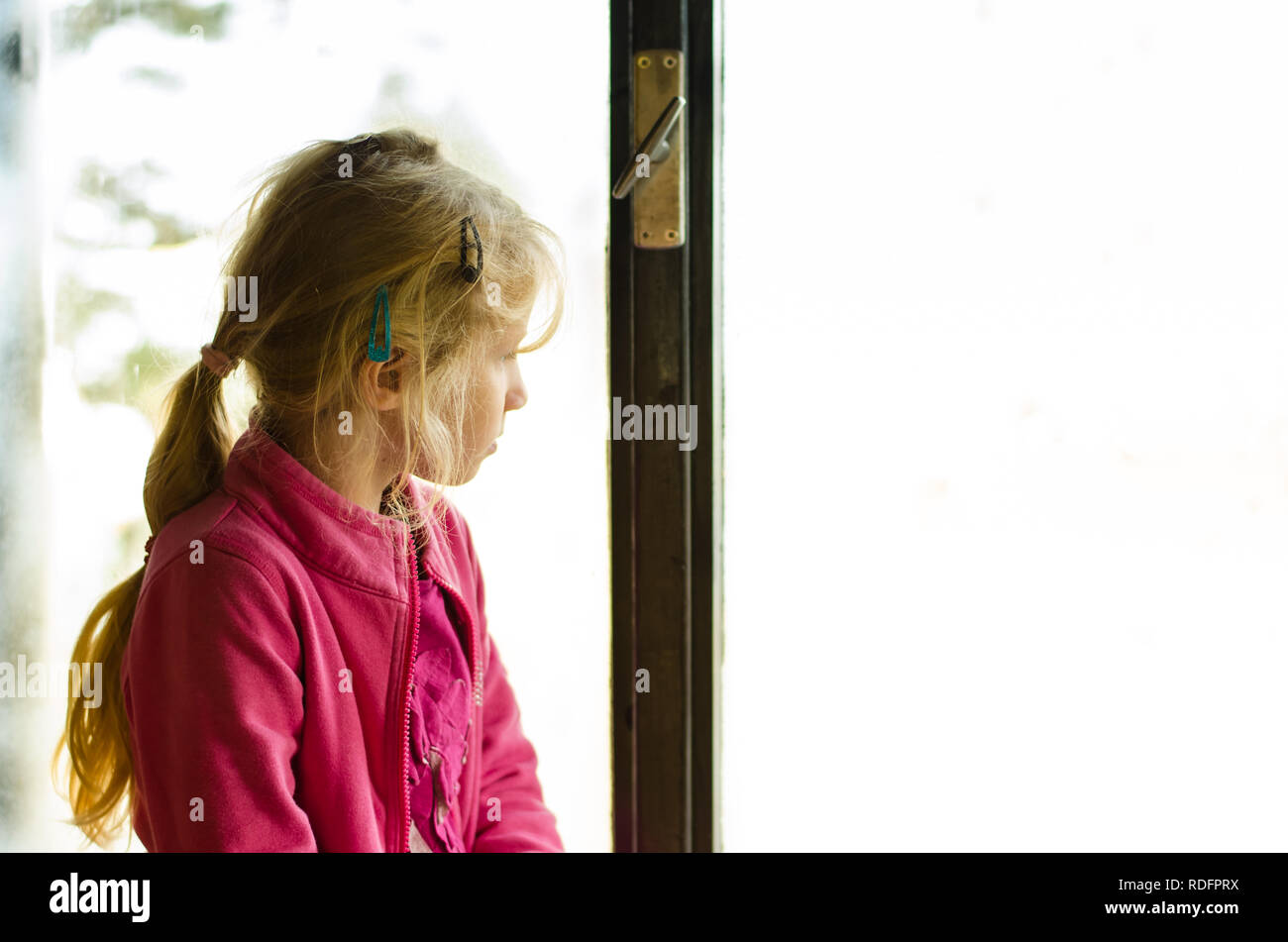 Bella ragazza bionda seduta dalla finestra e guardando al di fuori dello spazio di copia Foto Stock