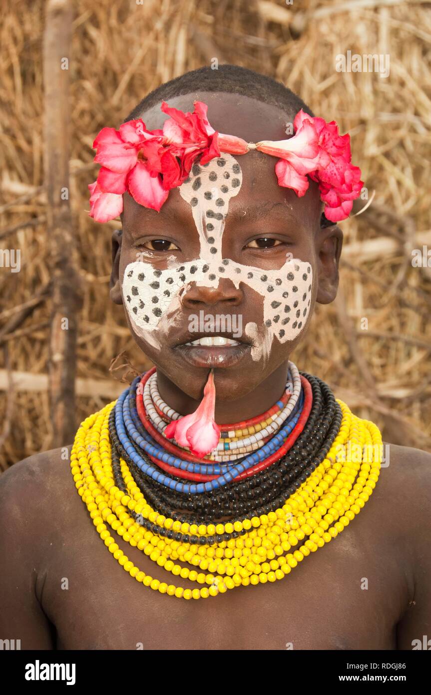 Karo ragazza con un archetto floreali, pitture facciali e colorati di collane e labbro piercing, Omo river valley, sud Etiopia Foto Stock