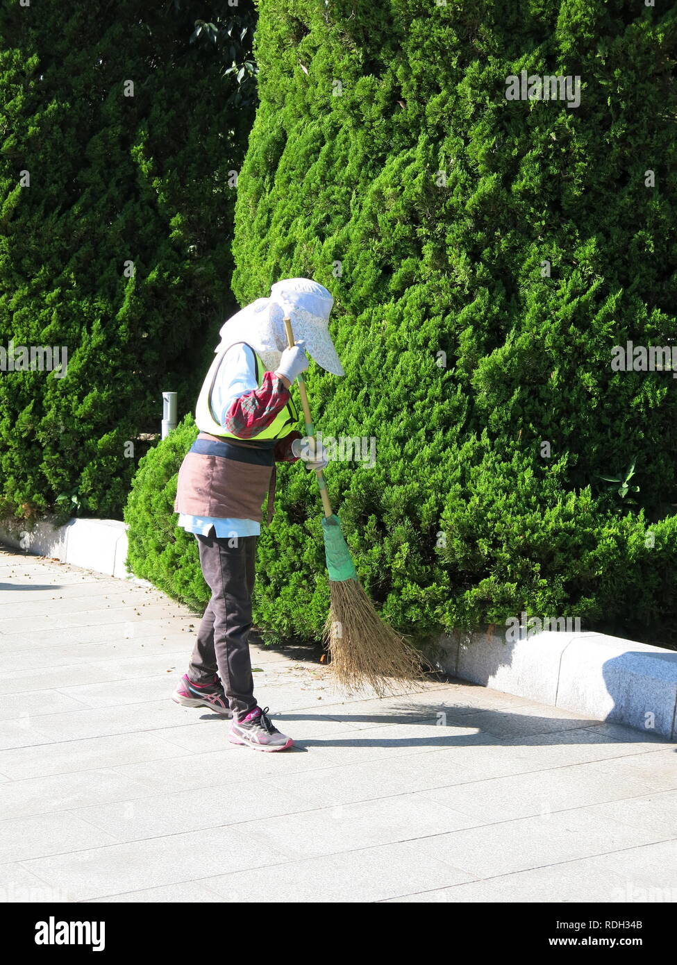 Vestito in giapponese ingranaggio di giardinaggio, una donna spazza i percorsi con una scopa nella motivazione dell'Hiroshima Peace Memorial Park. Foto Stock