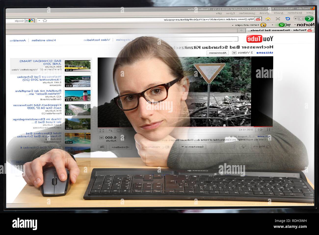 Giovane donna seduta a un computer per navigare in Internet, la visualizzazione di un video sul sito di YouTube, vista dall'interno del computer Foto Stock