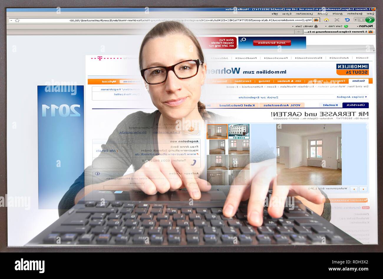 Giovane donna seduta a un computer per navigare in Internet, la visualizzazione di un sito immobiliare, immobilienscout24.de Foto Stock