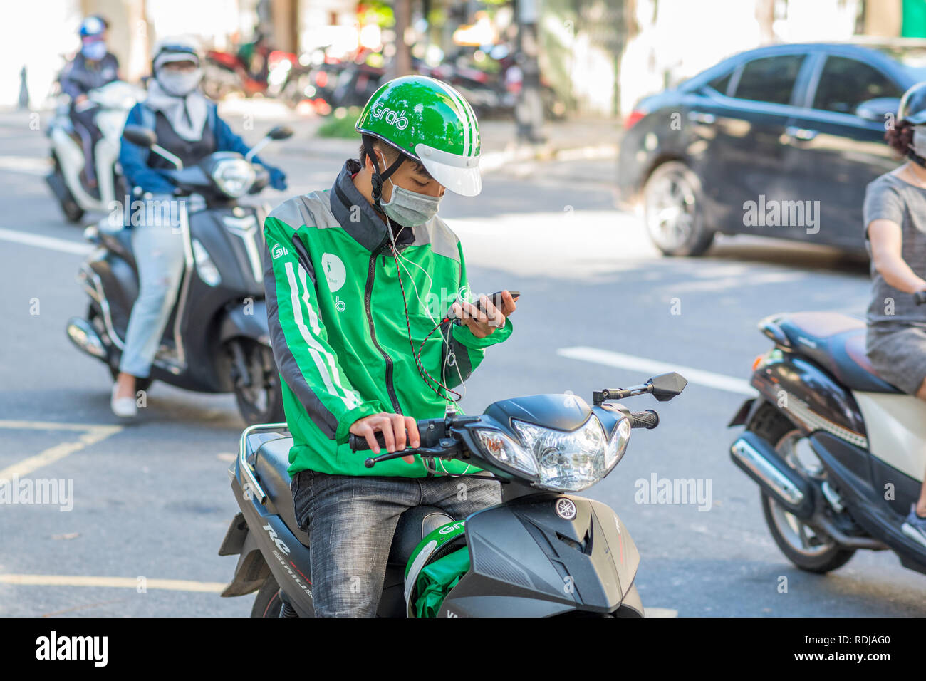 Danang, Vietnam - 14 Ottobre 2018: un giovane uomo su uno scooter, indossando un Grab verde casco e giacca, guarda al suo telefono mobile. Foto Stock