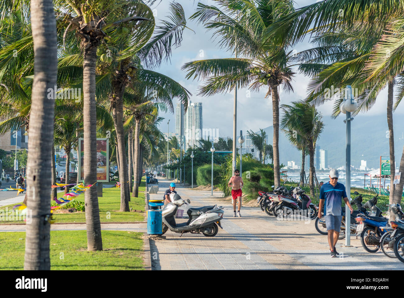 Da Nang, Vietnam: il marciapiede della via mare (Vo Nguyen Giap) lungo il mio Khe spiaggia con palme ondeggiano nel vento, persone sedersi, camminare, correre e mare. Foto Stock