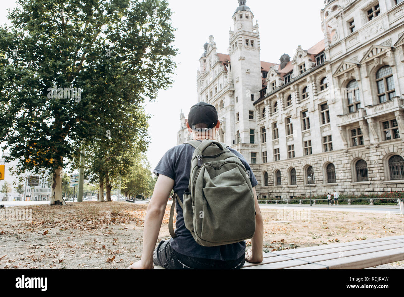 Un giovane uomo è seduta su una panchina lungo la strada di Lipsia in Germania ed è in appoggio. Foto Stock