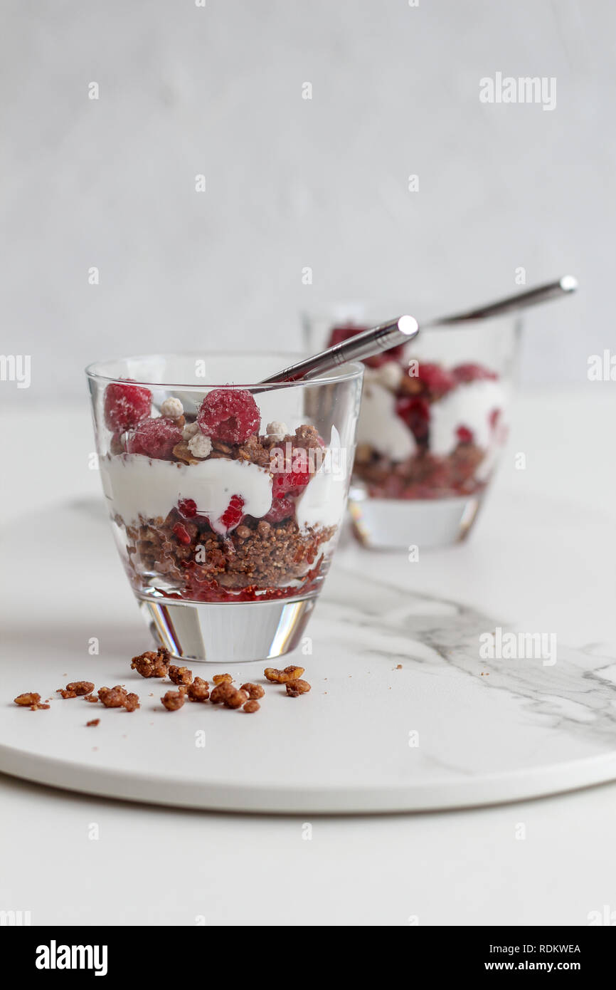 Due bicchieri di più livelli di cereali e yogurt con lamponi su un vassoio in marmo su sfondo bianco Foto Stock