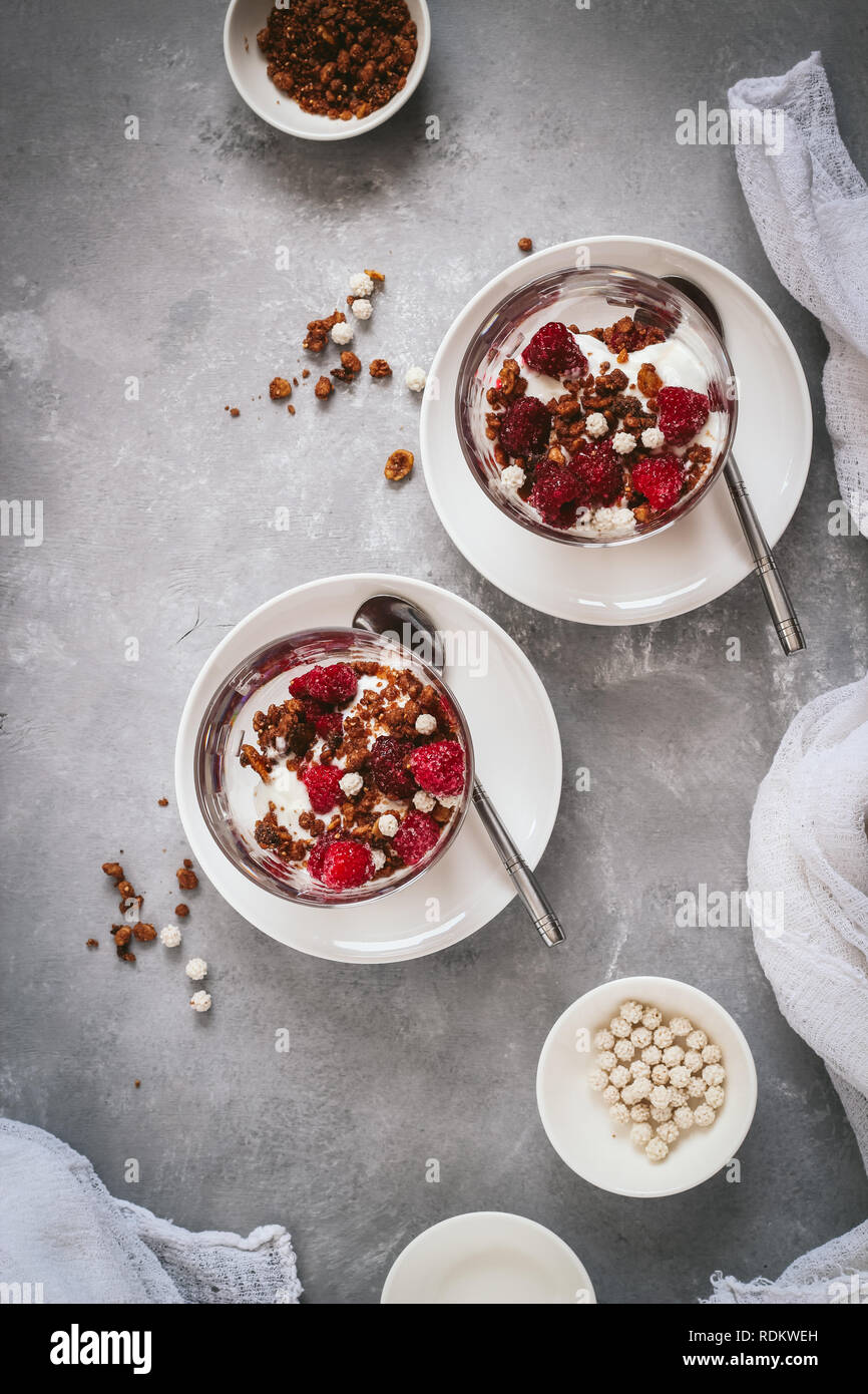 Lay piatto con vetri stratificati di cereali e yogurt con lamponi su sfondo scuro Foto Stock