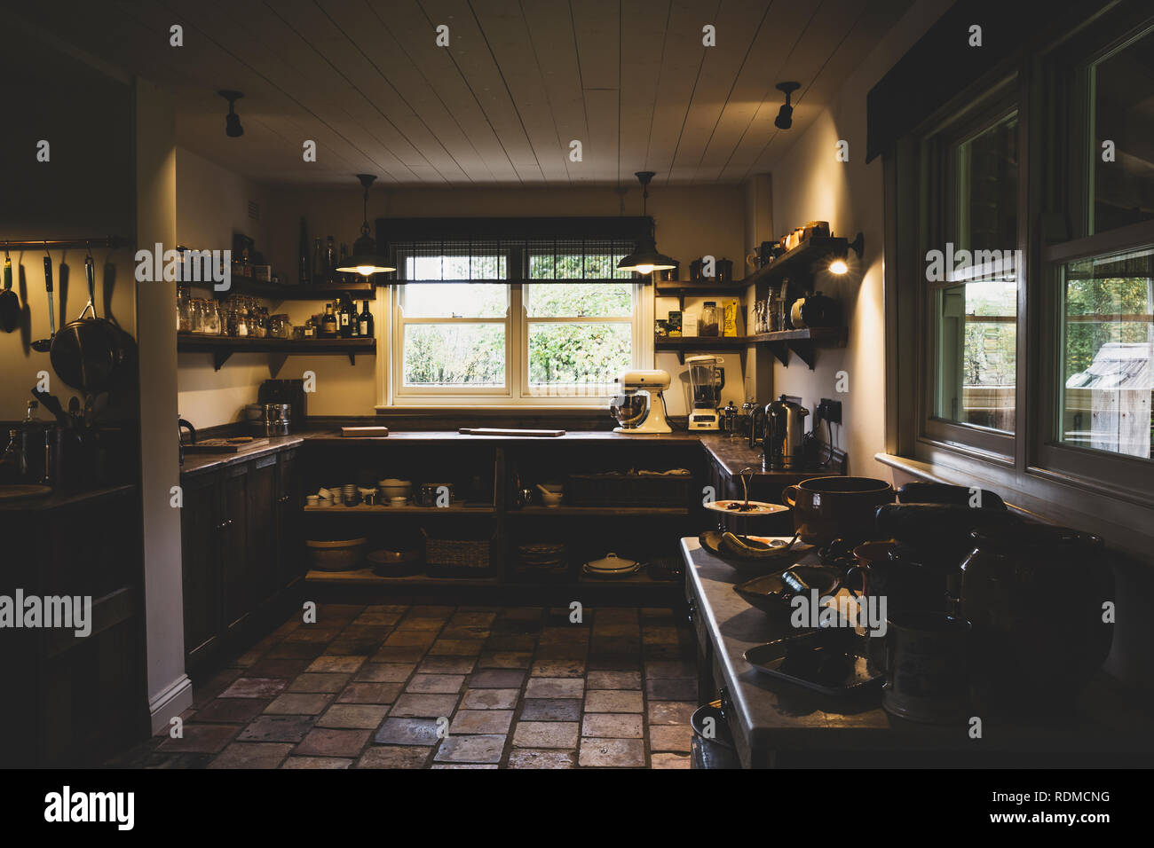 Vista interna della cucina con mattonelle in pietra pavimento, soffitto in legno e due finestre a ghigliottina, antiche in legno armadi e ripiani a parete. Foto Stock