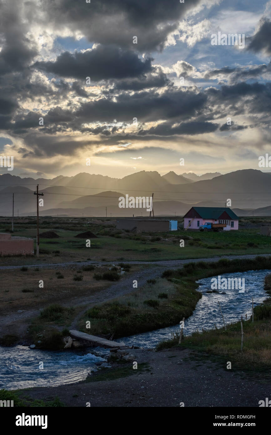 Sunset over cottage da un fiume con montagne distanti, sario con dossi, Kirghizistan. Foto Stock