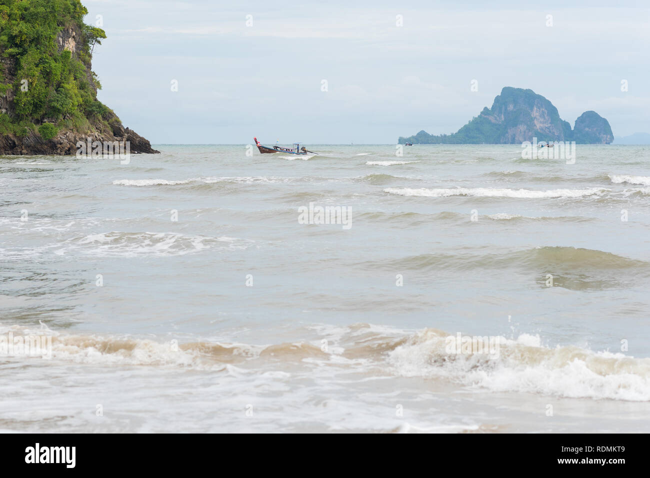 Mare ad Ao Nang Beach durante il ventoso nuvoloso giorno nella bassa stagione. Longtail barche e un'isola a distanza. Luglio a Krabi, Thailandia. Foto Stock