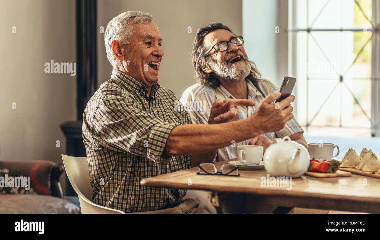 Alti uomini guardando le vecchie fotografie di loro nel telefono cellulare e ridere. Due uomini anziani guardando le vecchie fotografie insieme e ridere. Foto Stock