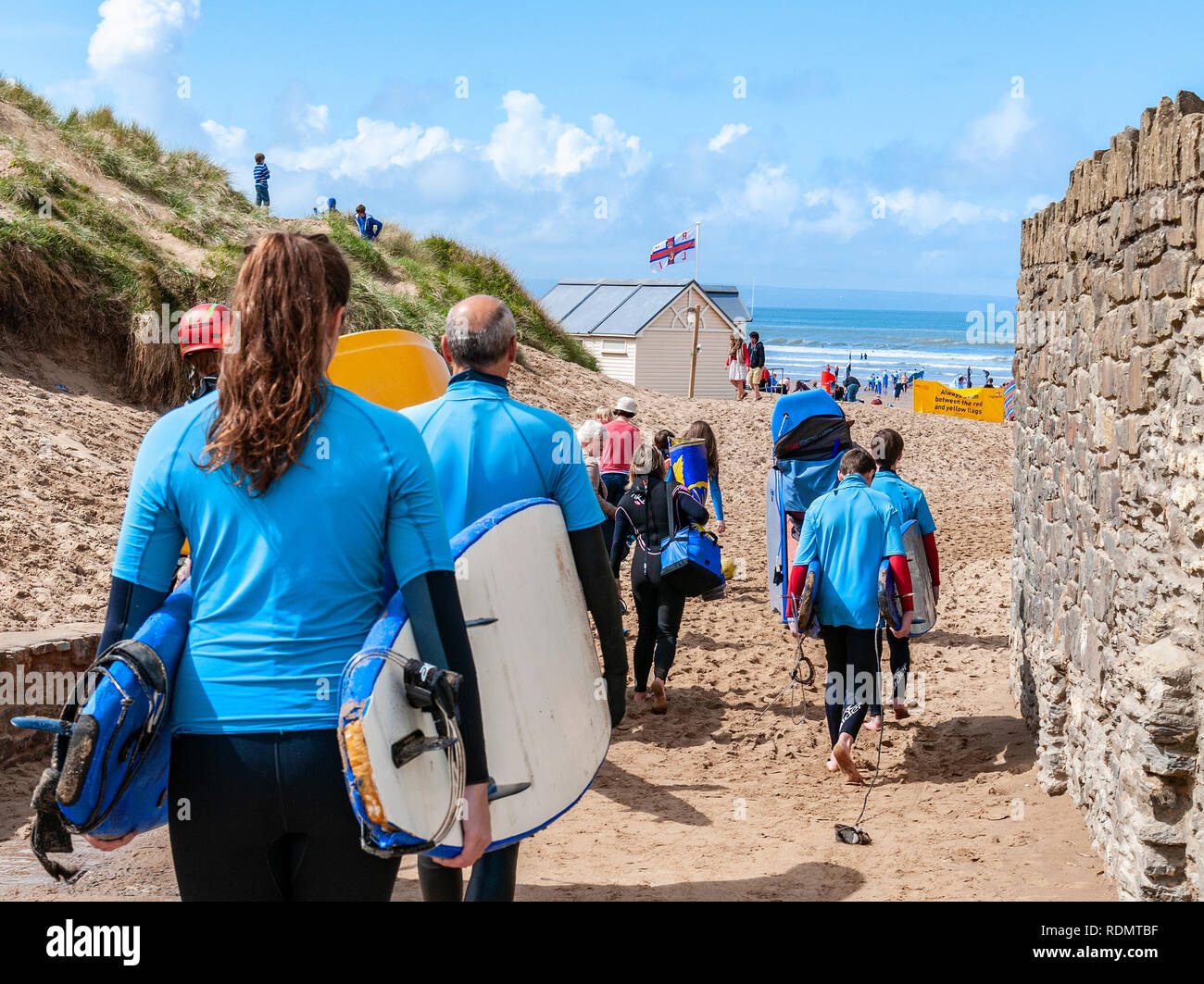 I surfisti camminano verso Croyde Beach, una famosa spiaggia di sabbia per il surf nel Devon del Nord, per fare una lezione di surf - Devon, Inghilterra, Regno Unito Foto Stock