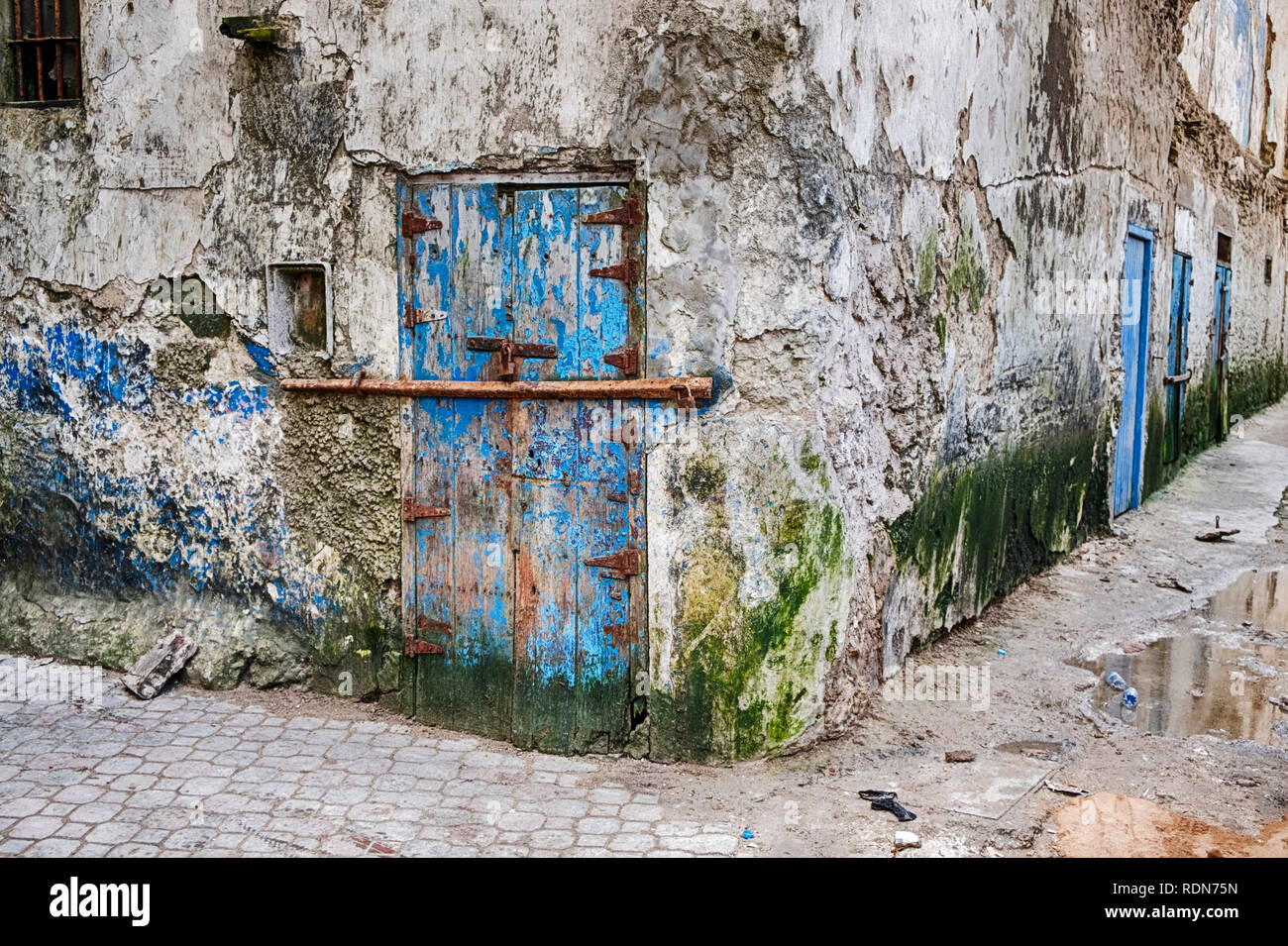 Un travagliato vecchio blu porta con un bar per la sicurezza in un malandato quartiere è situato in corrispondenza di un angolo di strada nella porzione Mellah Essaouira in Morocc Foto Stock