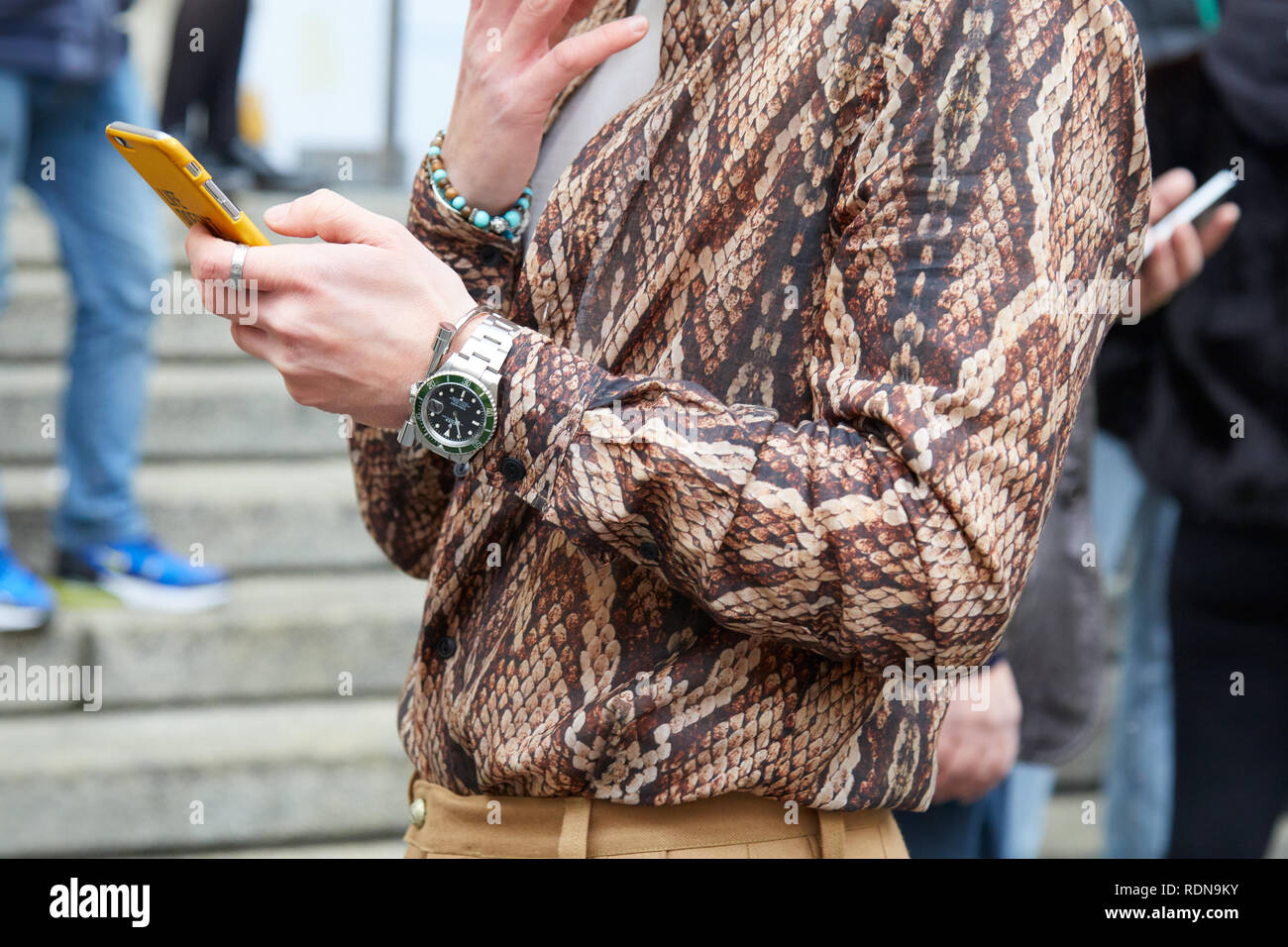 Milano, Italia - 12 gennaio 2019: uomo marrone con pelle di serpente maglietta stampa e Rolex Submariner watch guardando smartphone prima di Frankie Morello fash Foto Stock