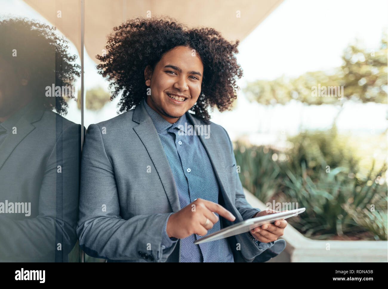 Giovani razza mista ragazzo con ricci afro cercando in azienda della fotocamera e puntando a un tablet Foto Stock