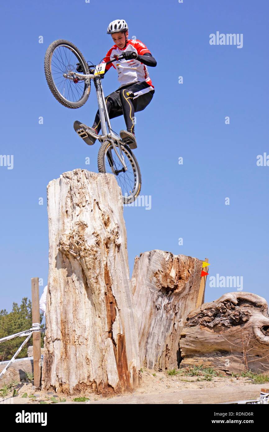 Adolescente saltando su un ceppo di albero con la sua moto ad una mountain bike trial Foto Stock