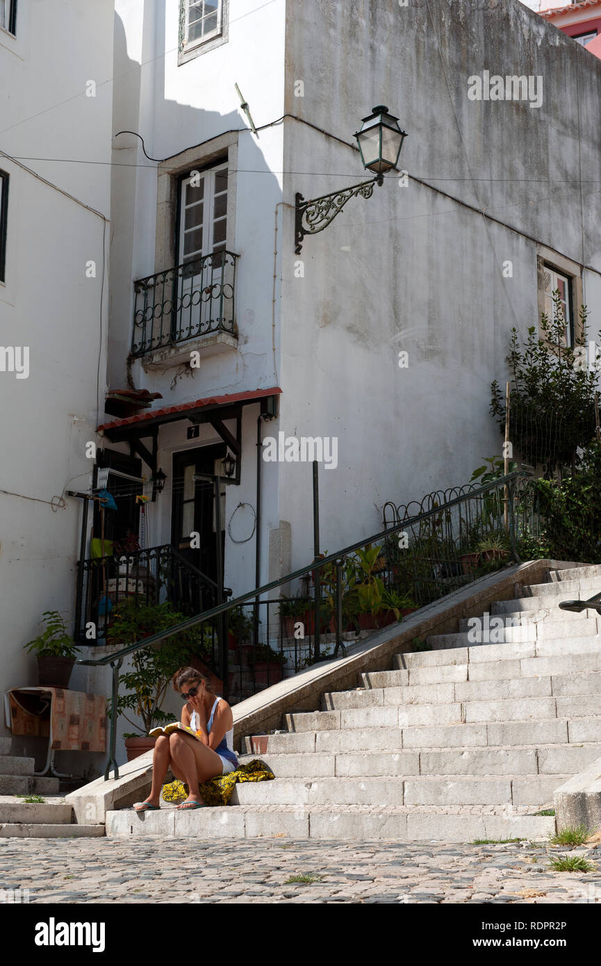 Una giovane donna leggendo un libro seduti sulle fasi di Alfama, Lisbona, Portogallo Foto Stock