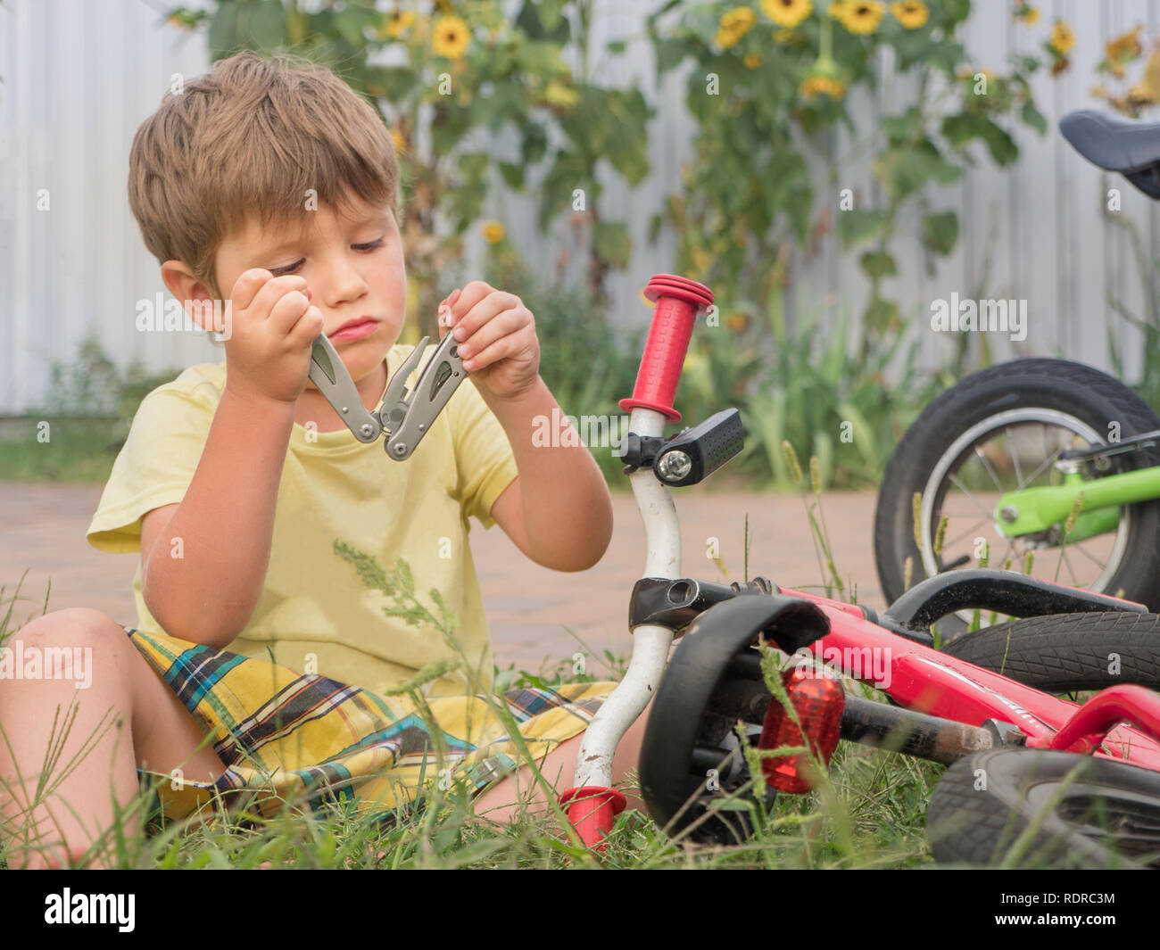 Apertura di capretto multi utensile durante la seduta vicino alla bicicletta. Fissaggio del ragazzo in bicicletta. Vacanze estive dello sfondo. Campi estivi sfondo. I trasporti e i bambini. C Foto Stock