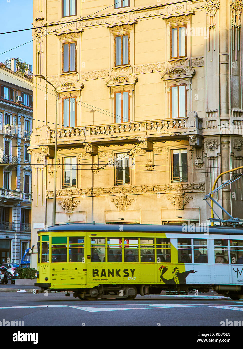 Un tram pubblicità una mostra monografica di Banksy attraversando Via Giovanni Boccaccio, una strada della zona quartiere Magenta nel centro di Milano. Foto Stock
